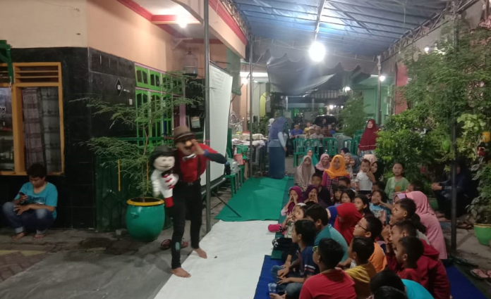 Pendongeng anak nasional Kak Harris dan bonekanya Ayis, tengah membawakan cerita dongeng kepada warga Teluk Aru 4, Surabaya